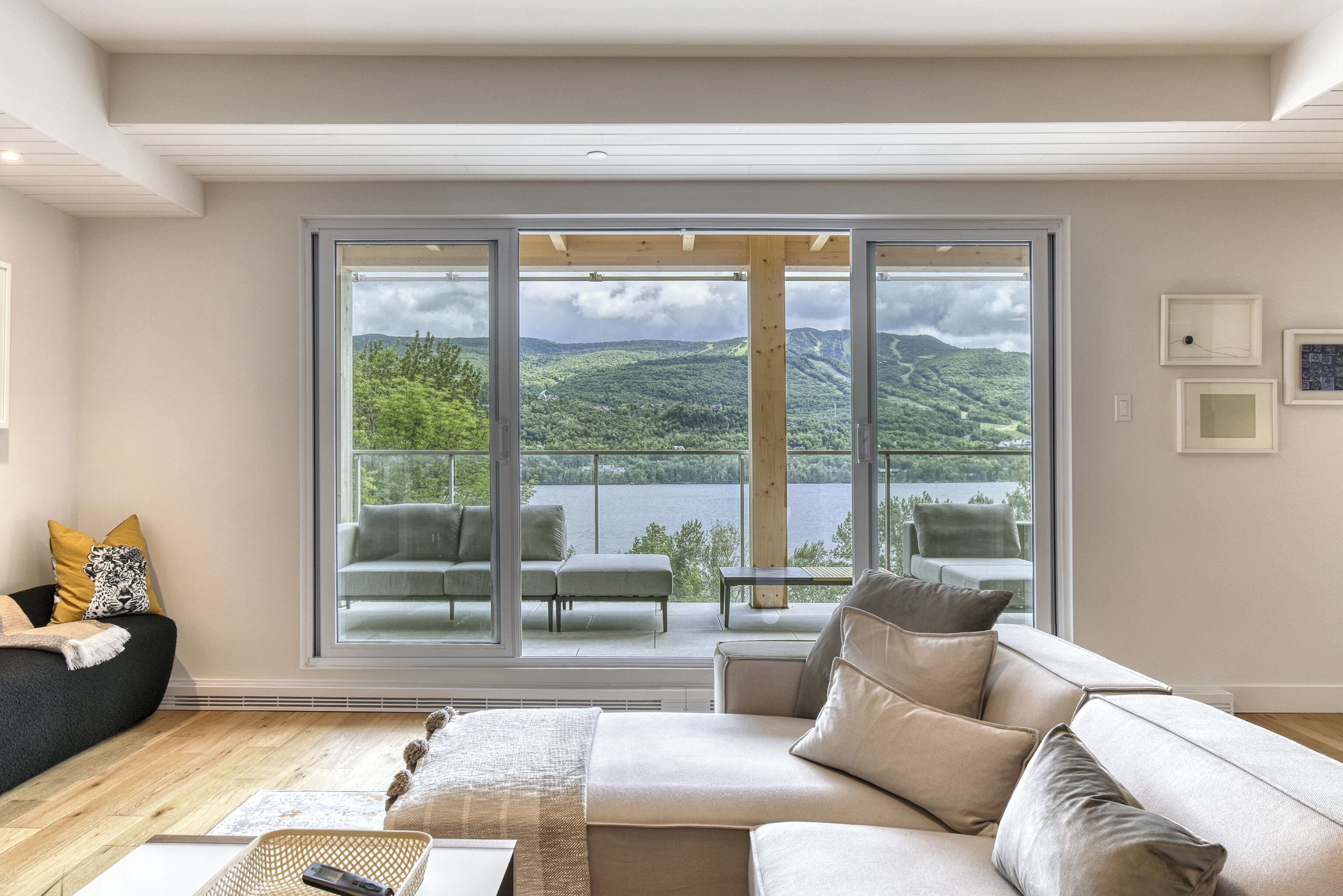 Ein modernes Wohnzimmer mit einem großen Schiebeglasfenster, das auf einen Balkon mit Blick auf einen See und Hügel führt.