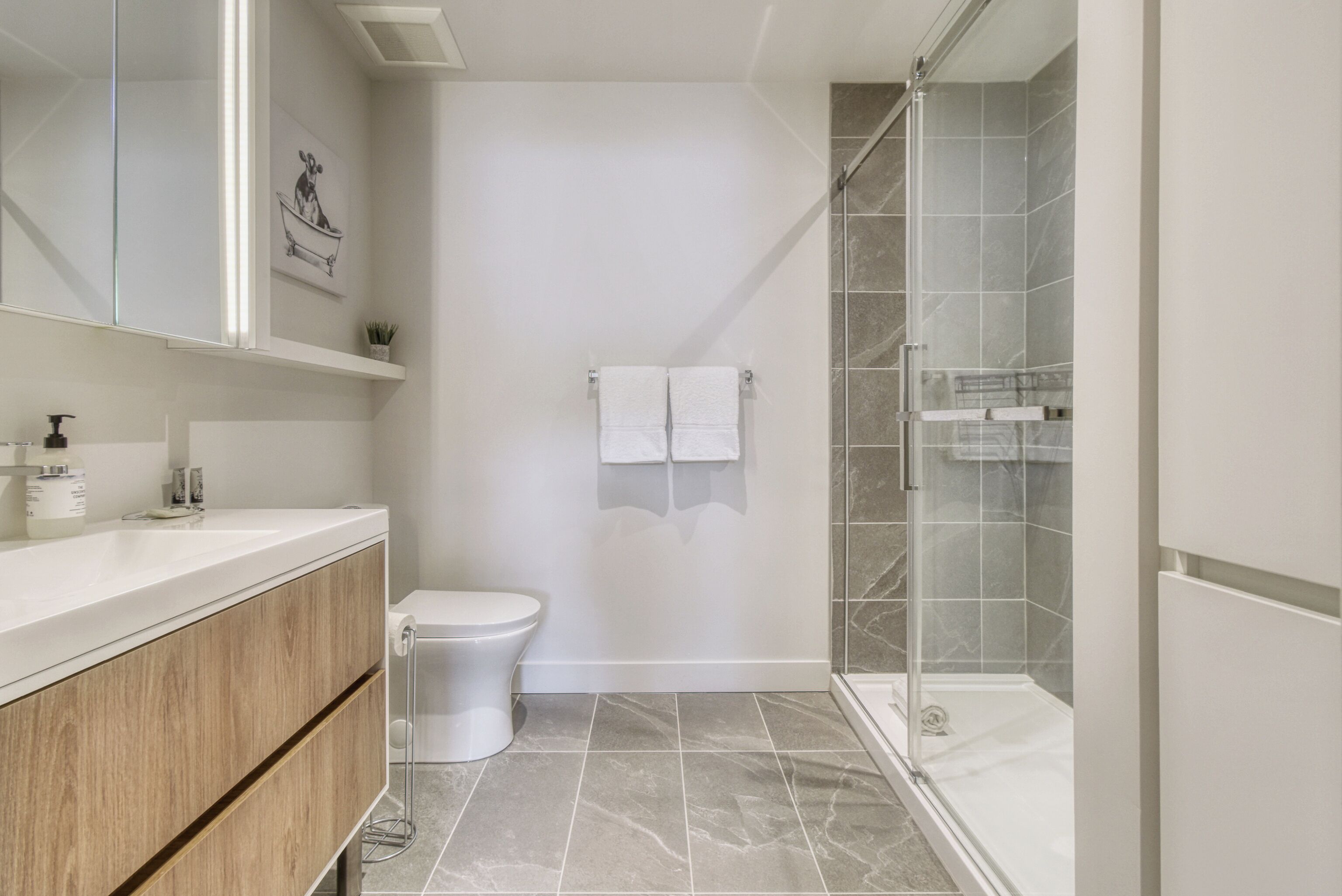 A modern bathroom with a white vanity, a toilet, a glass shower enclosure, and a marble-tiled floor.