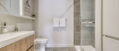 A modern bathroom with a white vanity, a toilet, a glass shower enclosure, and a marble-tiled floor.