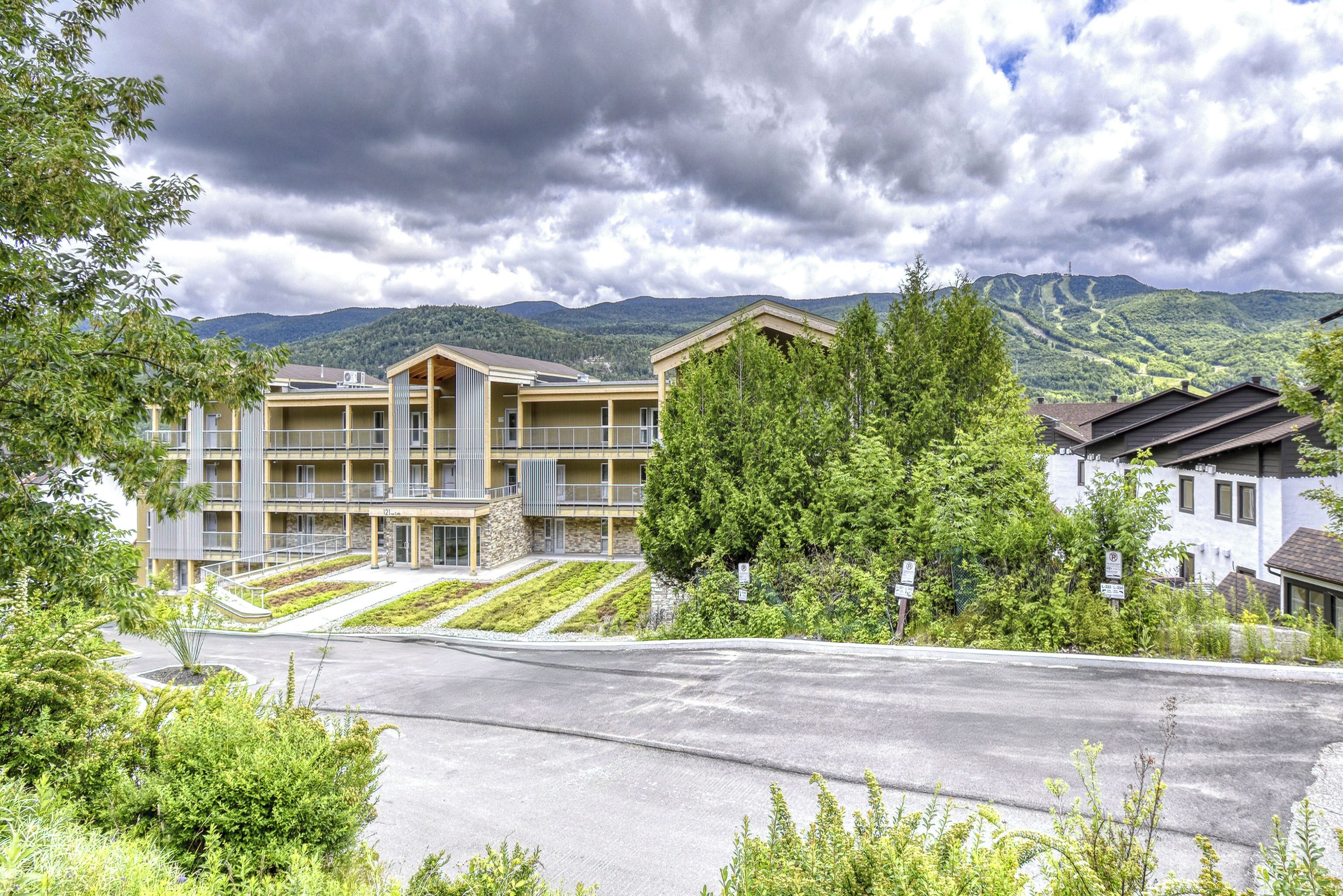 A modern building with a flat roof, multiple balconies, and a paved driveway.
