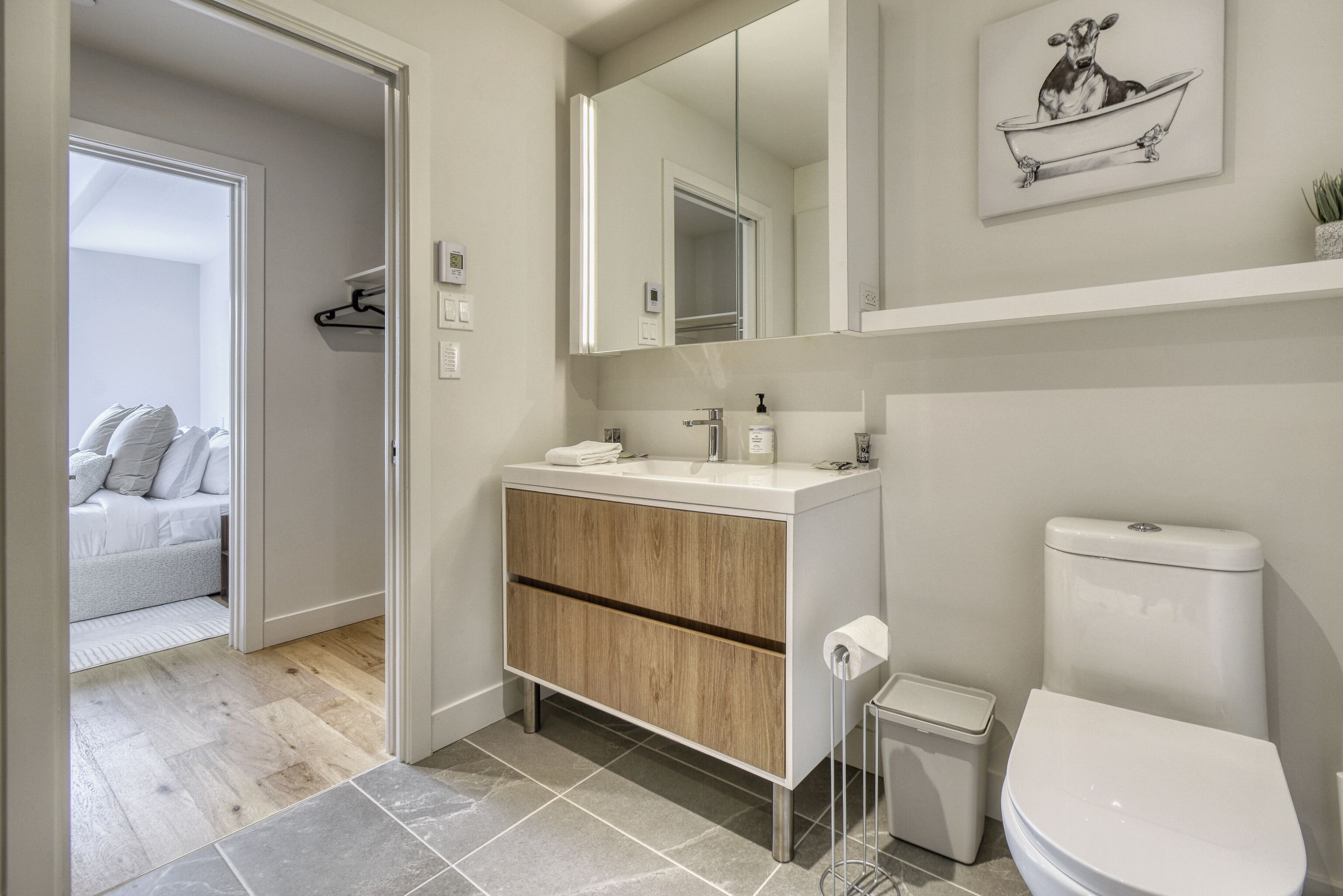 A modern bathroom with a wooden vanity, a white toilet, and a large mirror.