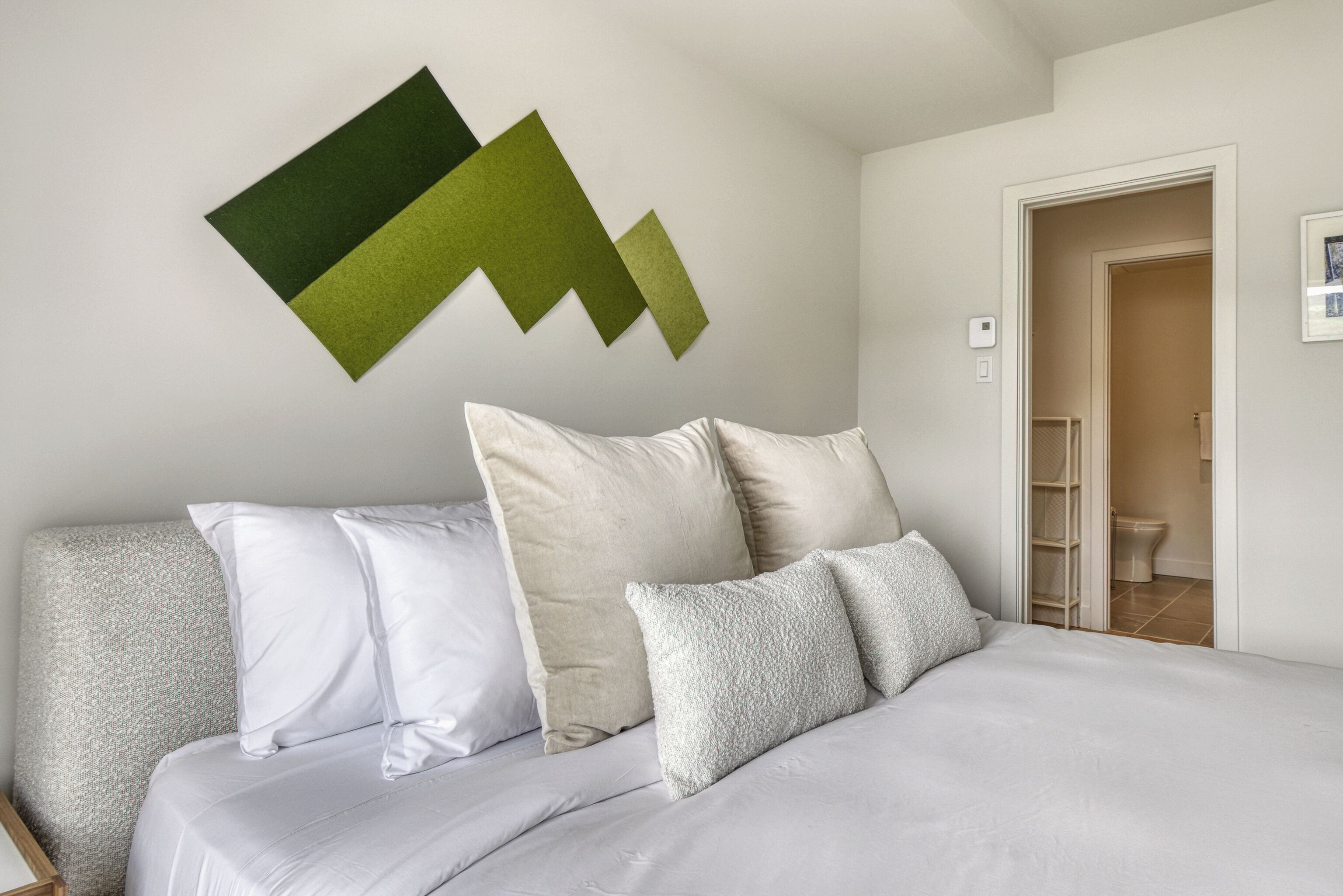 Una camera da letto con un letto, cuscini e un quadro astratto appeso al muro.