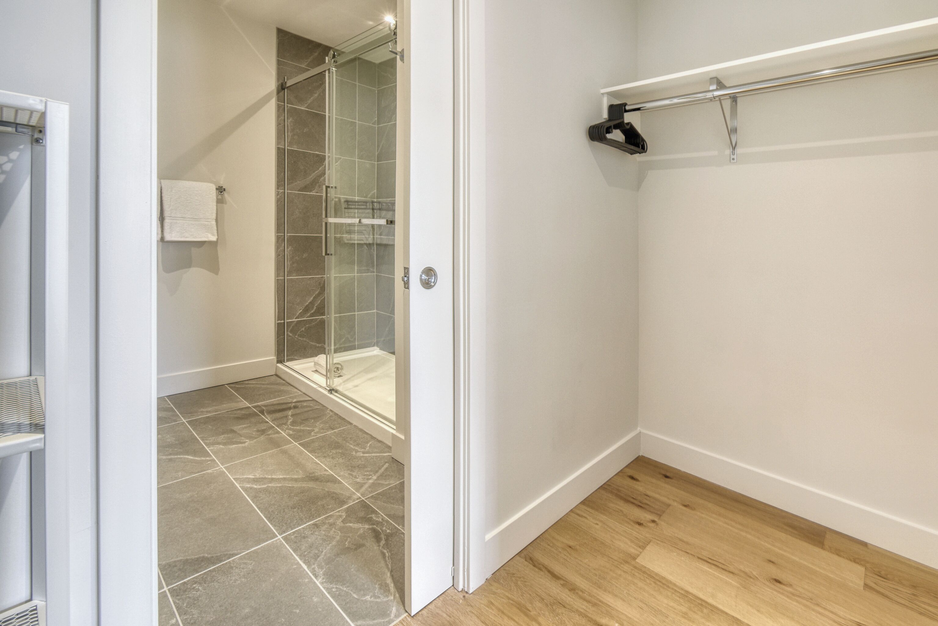 A bathroom with a glass shower enclosure, a white towel on a rack, and a wooden floor.