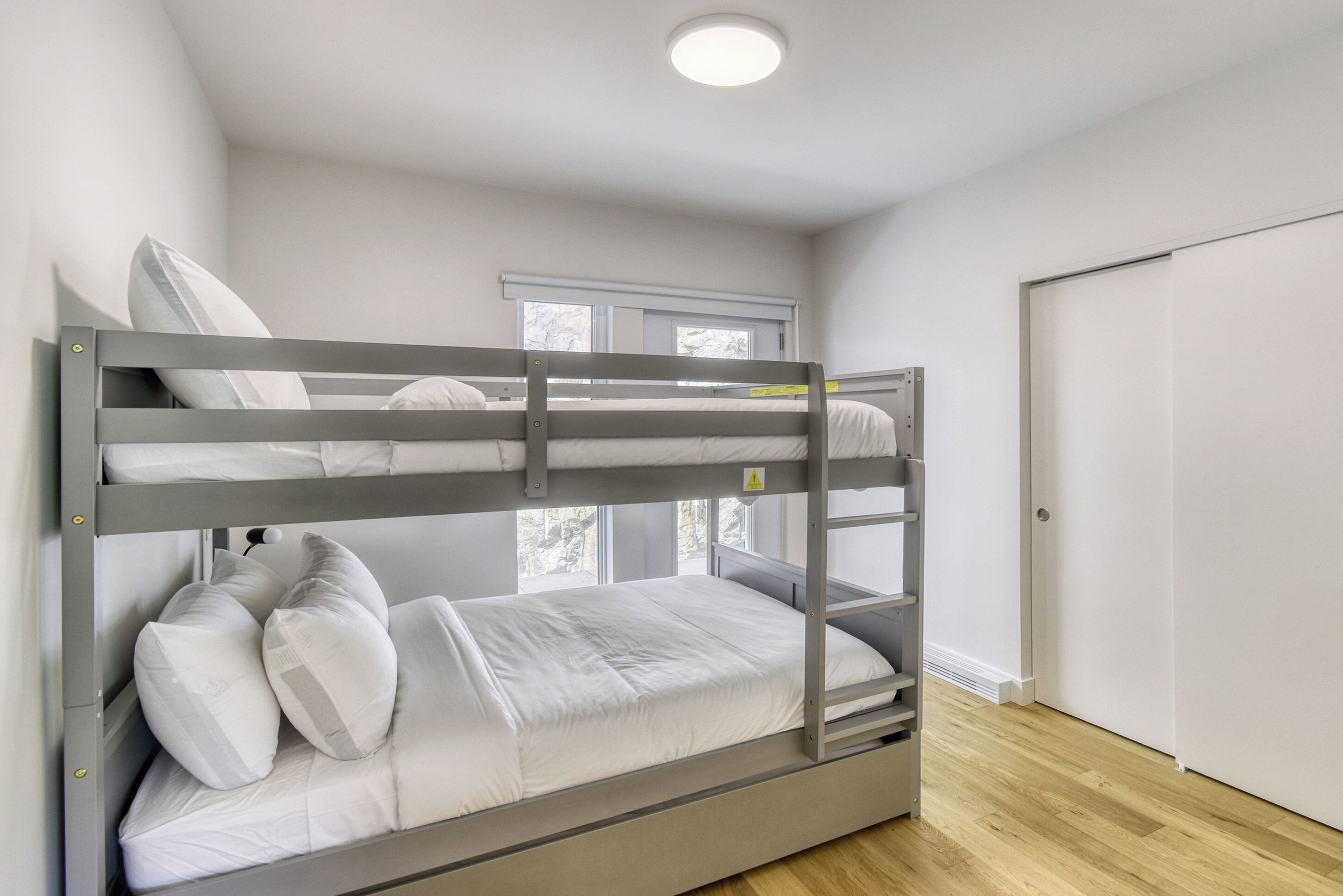 A bunk bed in a room with a wooden floor, a window, and a door.