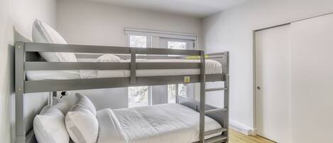 Una cama individual superpuesta en una habitación con suelo de madera, una ventana y una puerta.