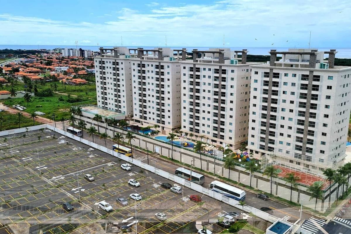 A high-rise building with multiple floors, a parking lot in front, and a view of the ocean.