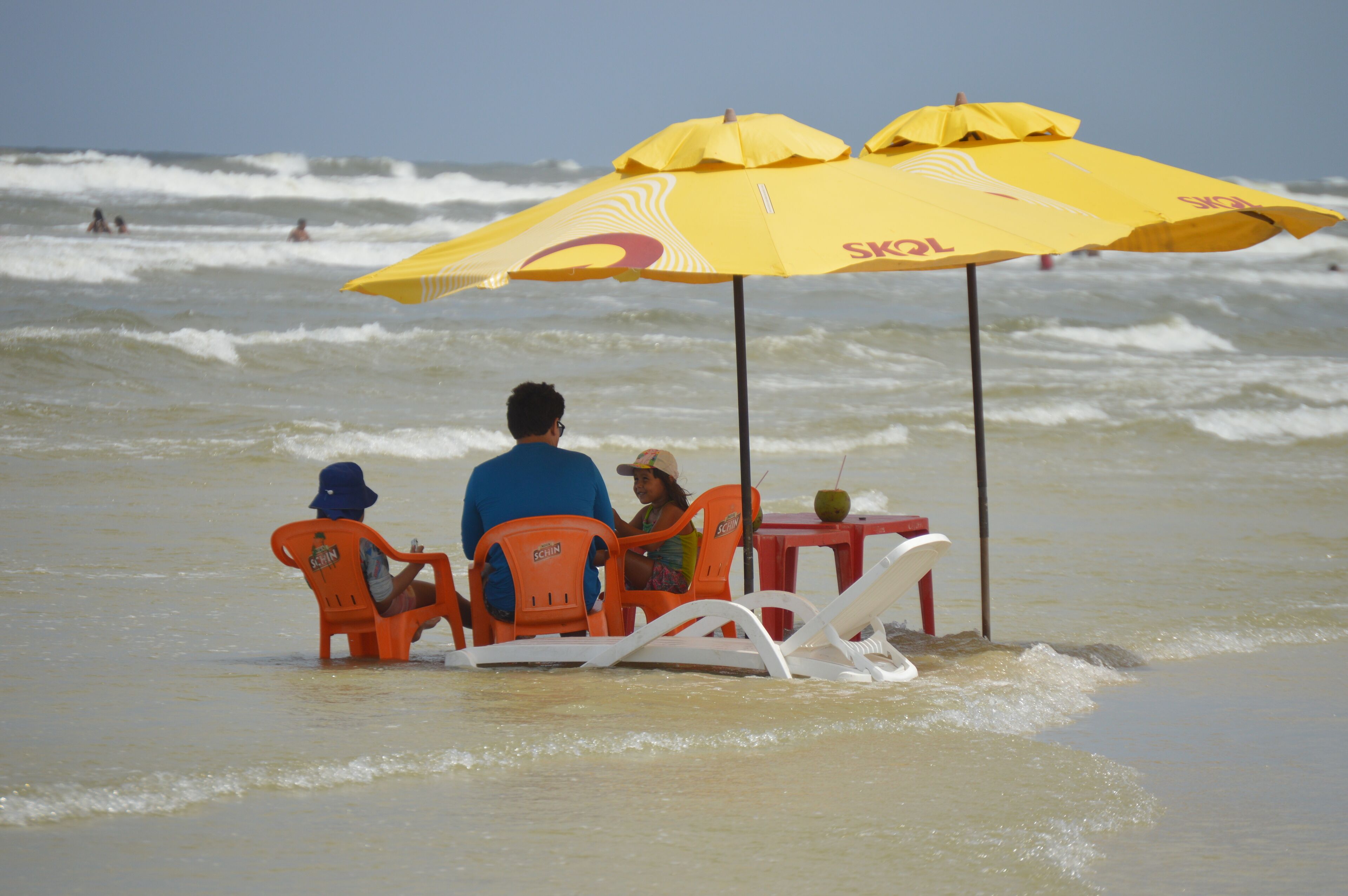 A beach scene with a table and chairs under a yellow umbrella.