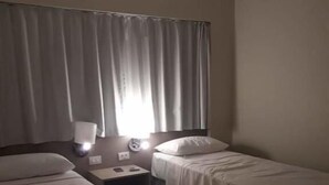 A hotel room with two single beds, a nightstand with a lamp, and a window with curtains. - SaltBeach - Salinas Park Resort (Salinópolis)