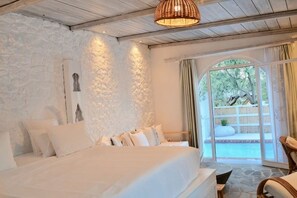 Une chambre avec un grand lit, des murs en pierre, un luminaire suspendu en osier et une vue sur l’extérieur, visible à travers une porte vitrée.