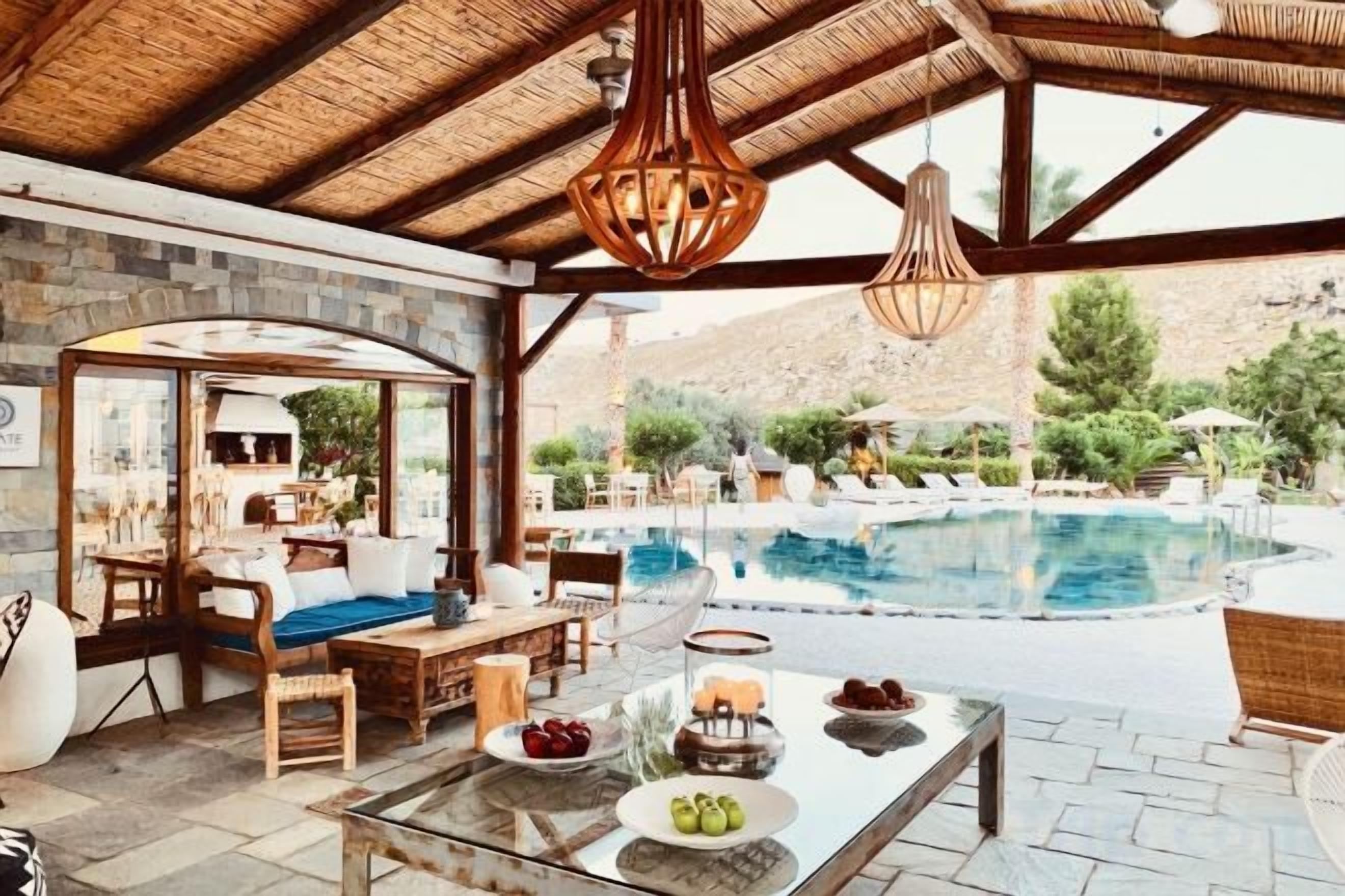 Zona de piscina exterior con área de descanso techada, una mesa con fruta y un bar.