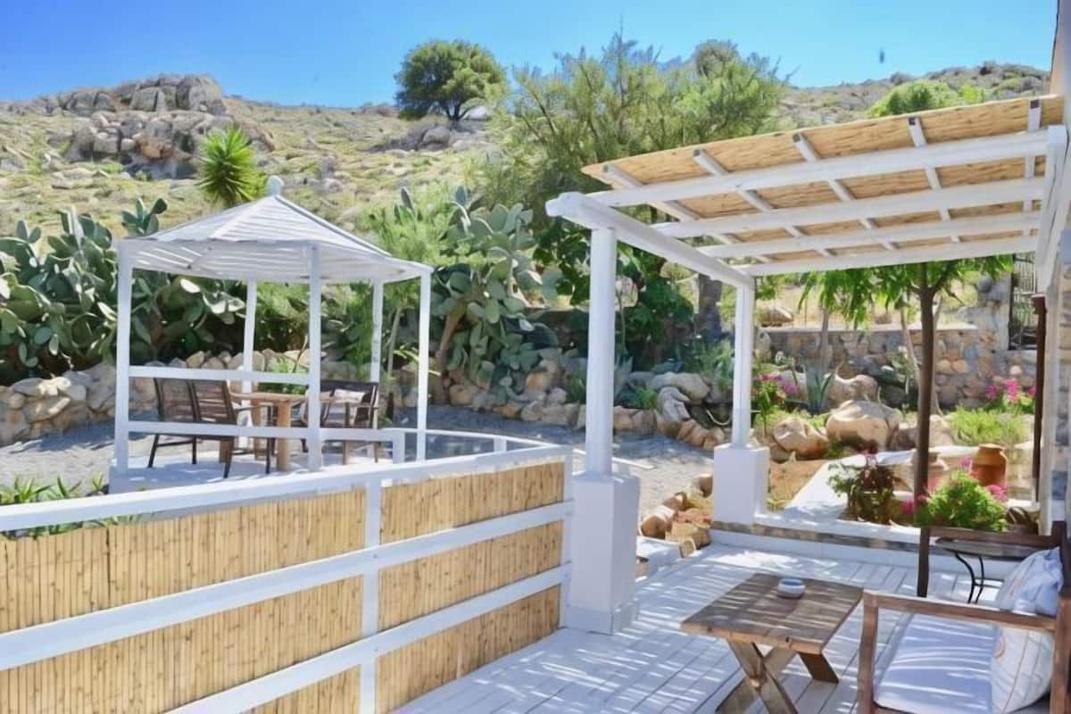 Ein überdachter Außenbereich mit Pergola, einem Holztisch und Stühlen.