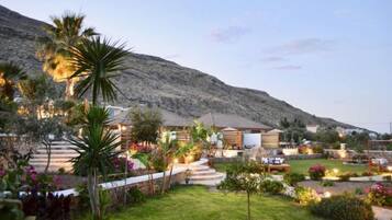 A hotel with multiple buildings, a well-maintained garden, and a mountain in the background.