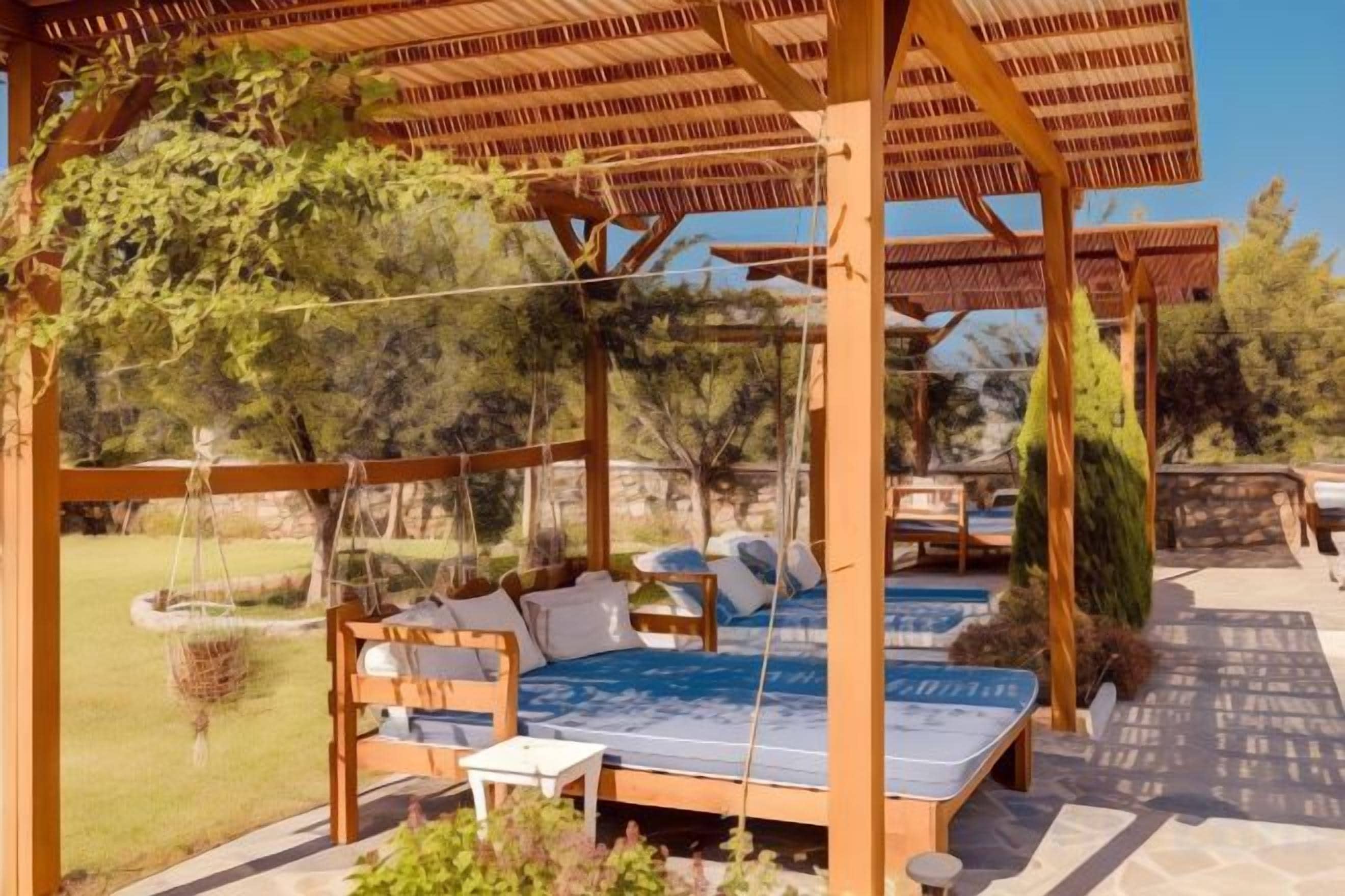 Una pérgola de madera con una hamaca colgante y una cama con colchón azul.