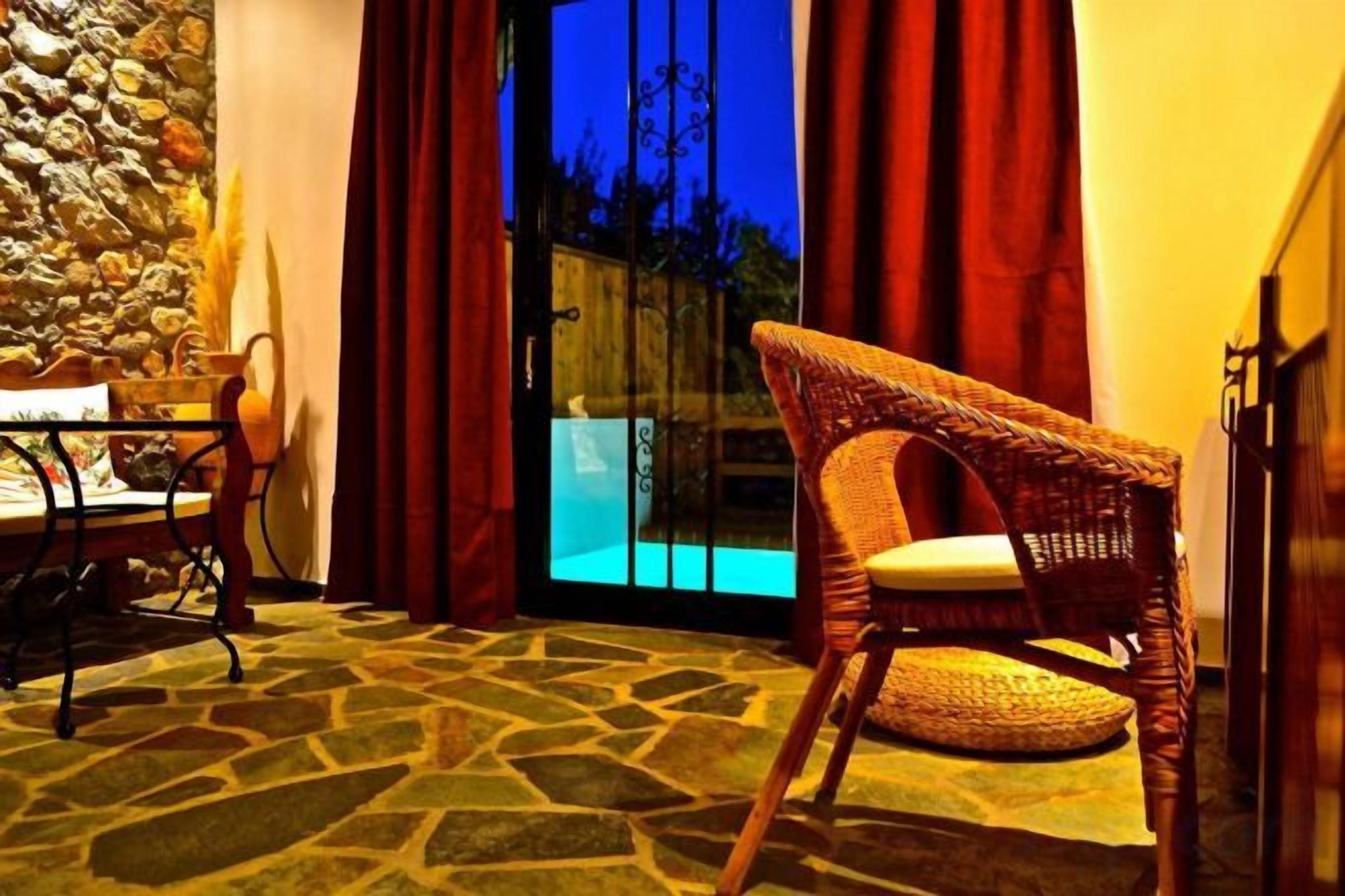 A wicker chair with a cushion, a table with a basket, and a stone-patterned floor.