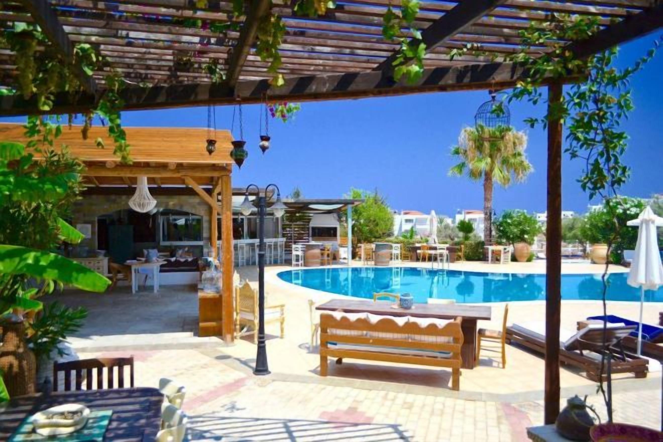 A poolside area with a wooden pergola, lounge chairs, and a pool.