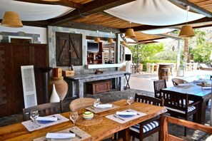 An outdoor dining area with wooden tables and chairs, a stone fireplace, and hanging lights. - Caesars Gardens Hotel & Spa - Adults Only (Rhodes)