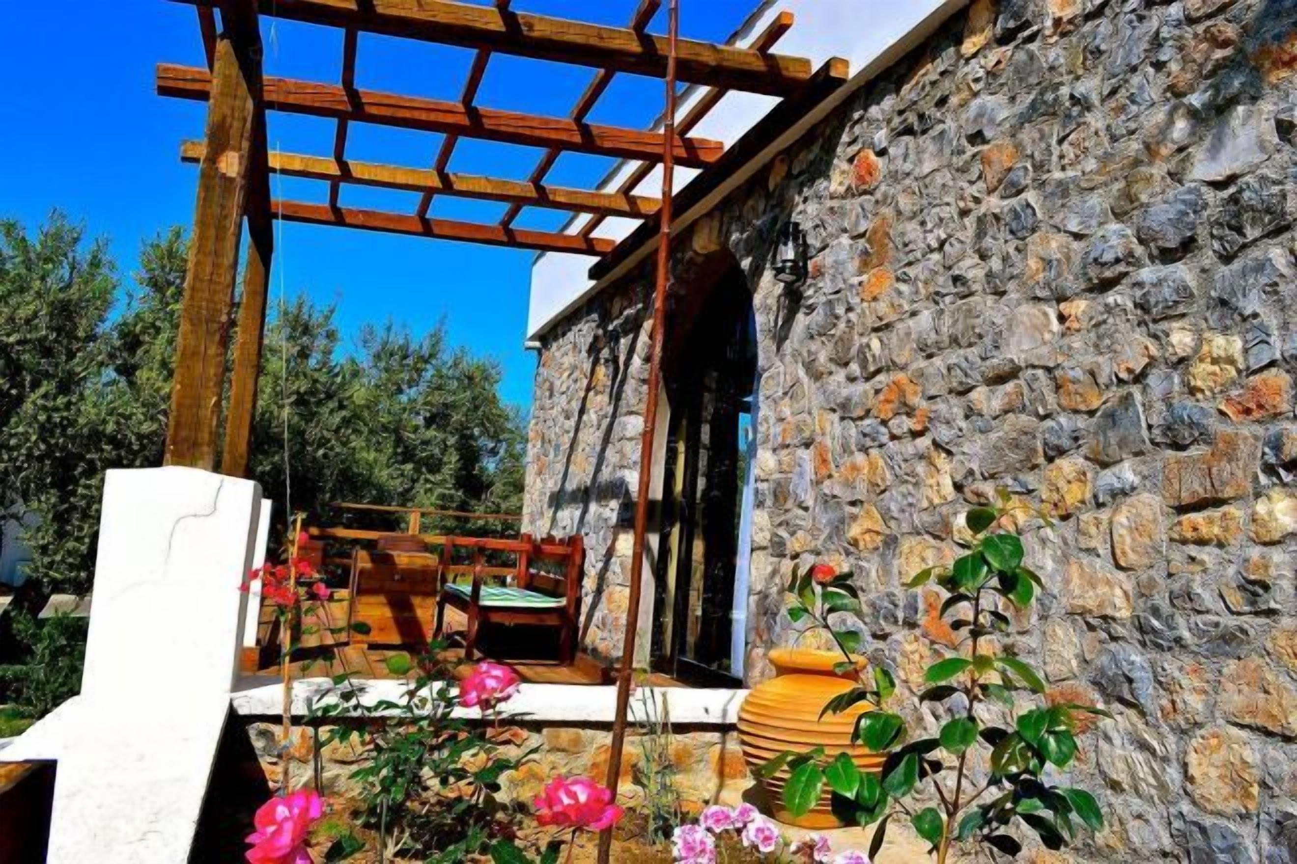 Un edificio de piedra con una pérgola de madera y un jardín lleno de flores.