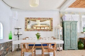 Un coin repas avec une table blanche, des chaises en bois, un miroir décoratif et un meuble vert.