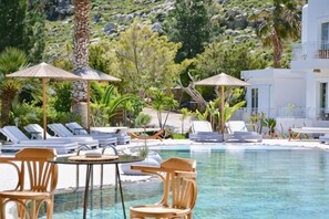 Un área de piscina con sillones, sombrillas y una mesa.