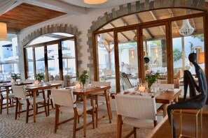 A restaurant with wooden tables and chairs, large windows, and a view of the outdoors. - Caesars Gardens Hotel & Spa - Adults Only (Rhodes)