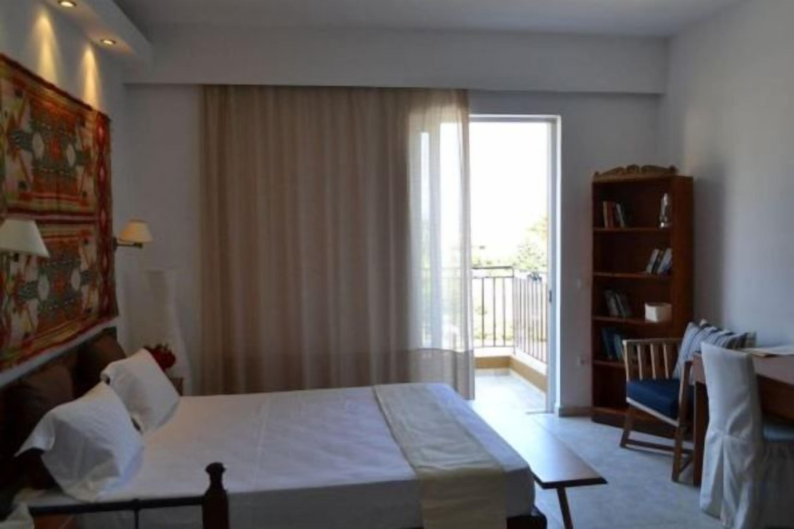 Una habitación de hotel con una cama, una estantería, una ventana con cortinas y vistas al exterior.