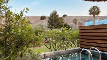 A swimming pool with a wooden deck and metal ladder, surrounded by greenery and a hilly landscape.