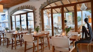 A restaurant with wooden tables and chairs, large windows, and a stone wall.