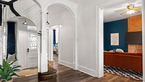 A hallway with a wooden floor, white walls, and a blue accent wall. There is a round rug on the floor, a plant in a basket, and a ceiling fan.