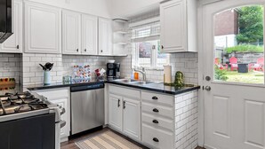 A kitchen with white cabinets, a dishwasher, a stove, and a window with a view of a garden.