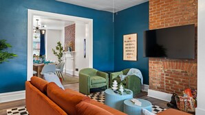 A living room with a blue wall, a brick fireplace, a flat-screen TV, green chairs, and a sofa.