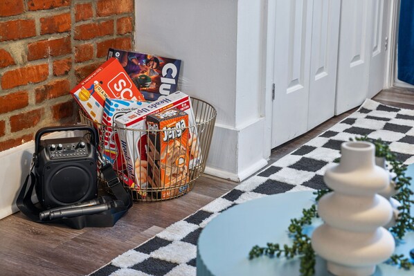 A room with a checkered floor, a small round table with a vase, a basket of board games, and a speaker.