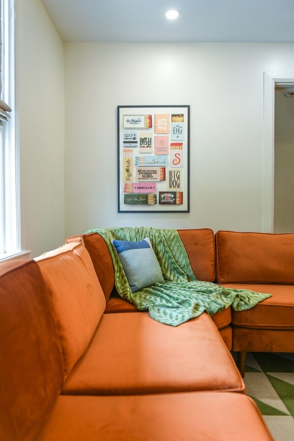A room with an orange leather sofa, a framed poster on the wall, and a window to the left.