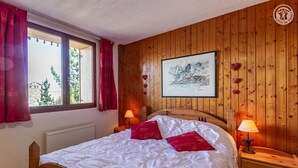 A wooden-paneled bedroom with a bed, two bedside tables, a window with curtains, and a framed picture on the wall.
