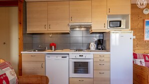 A compact kitchen with wooden cabinets, a microwave, a coffee maker, and a dishwasher.
