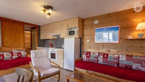 A cozy cabin-style room with a kitchenette, a sofa with a red blanket, a wooden chair, and a small table.