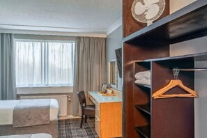 Una habitación de hotel con cama, escritorio, silla, armario y ventana con cortinas.