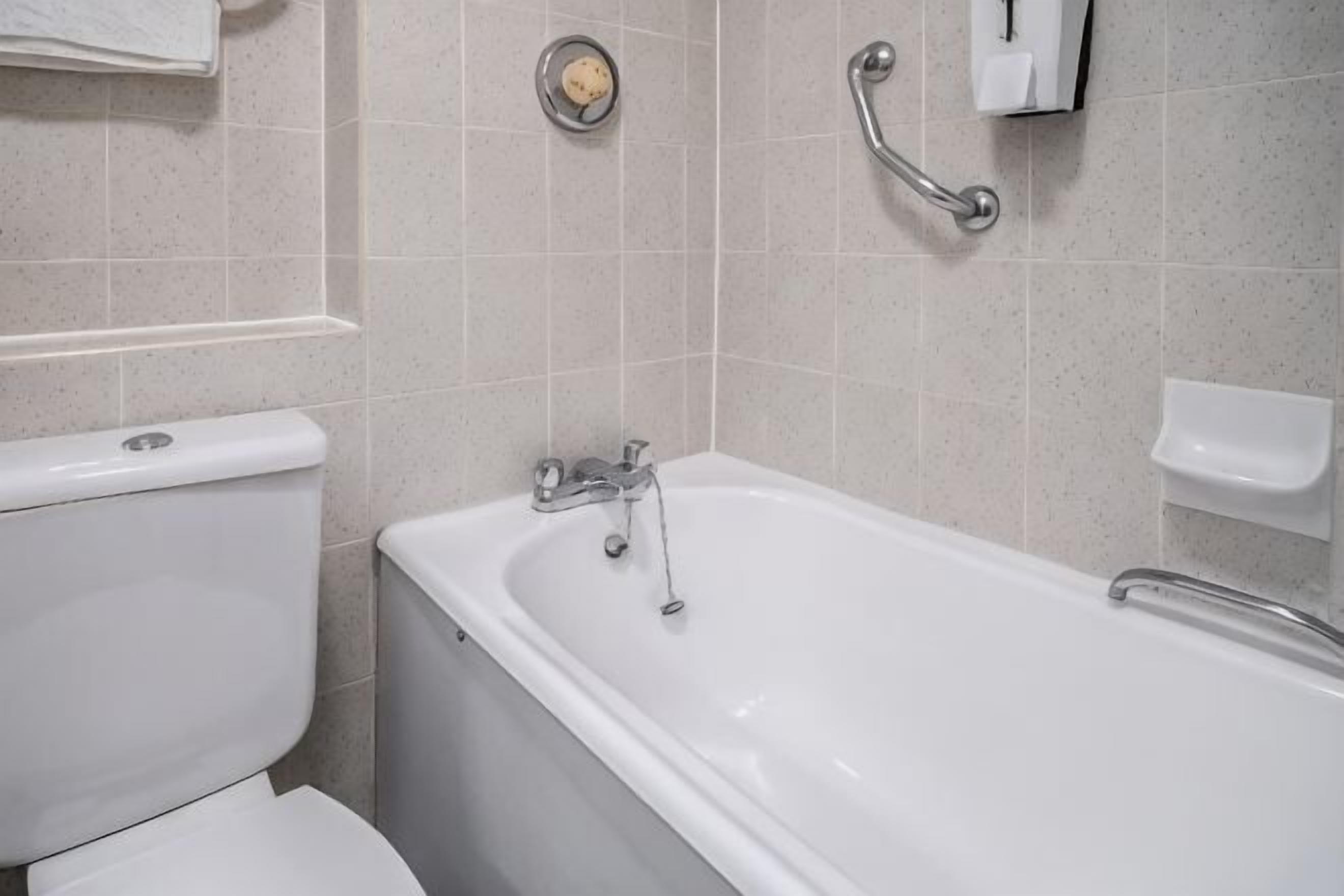 Un bagno con il water, una vasca e una maniglia di sostegno.