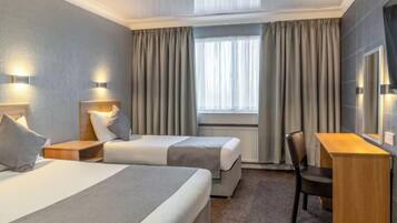 A hotel room with two beds, a desk, a chair, and a large window with curtains.