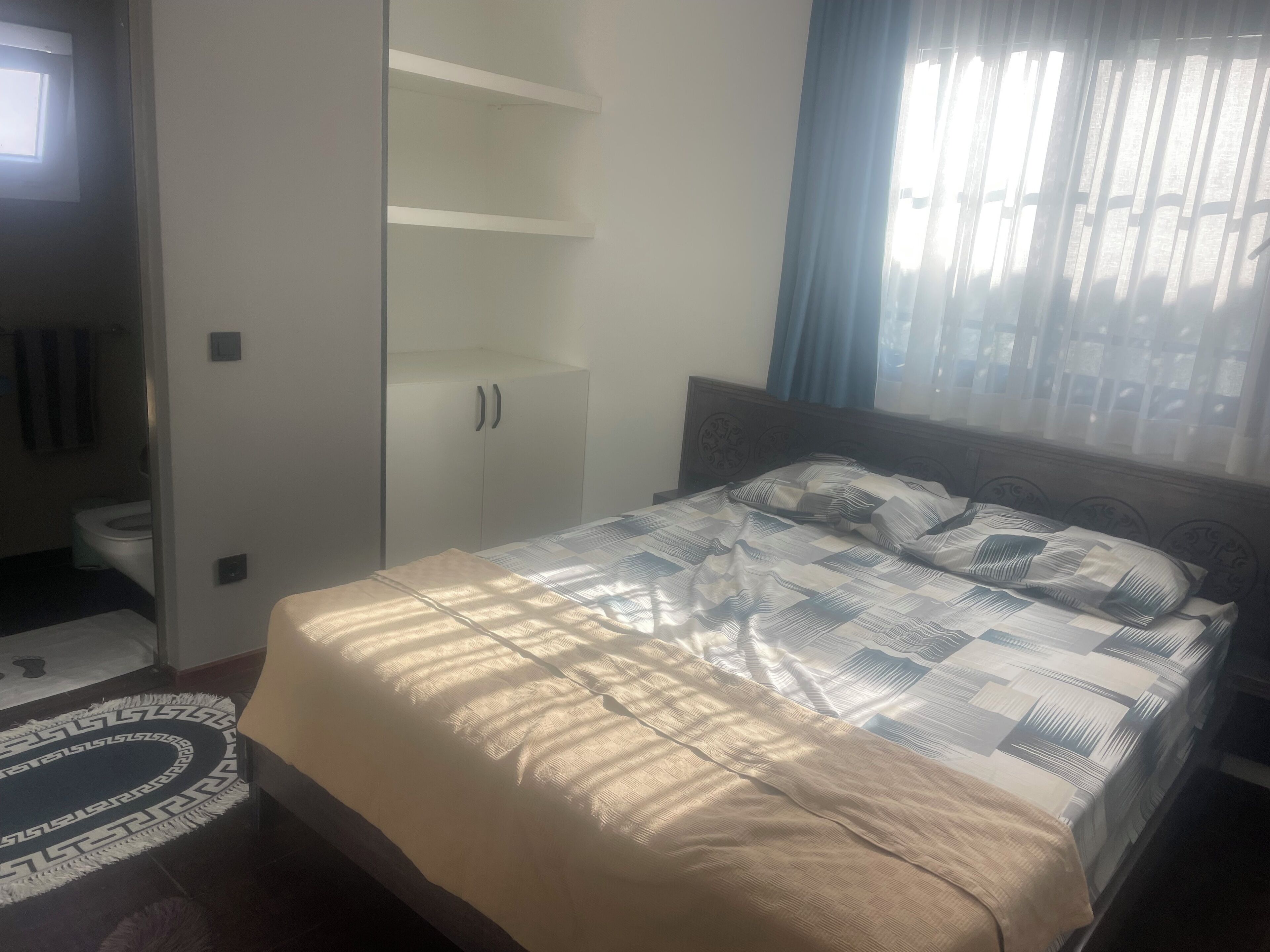 Un dormitorio con cama, armario y ventana con cortinas.