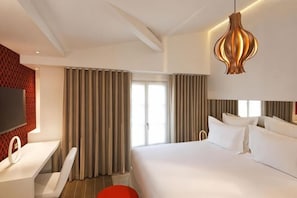 A hotel room with a large bed, a desk, a chair, a TV, and a large window with curtains. - Hotel Dupond-Smith (Paris)