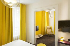 Et hotelværelse med seng, fjernsyn, stol og skrivebord med lampe.