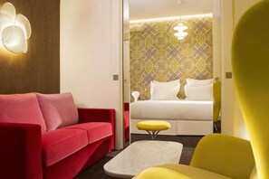 A modern hotel room with a red sofa, a yellow armchair, a white bed, and a patterned wallpaper. - Hotel Dupond-Smith (Paris)