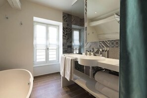 A modern bathroom with a freestanding bathtub, a vanity with a mirror, and a window providing natural light. - Hotel Dupond-Smith (Paris)