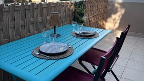Un área de comedor al aire libre con una mesa azul dispuesta para dos personas, rodeada de sillas de mimbre.