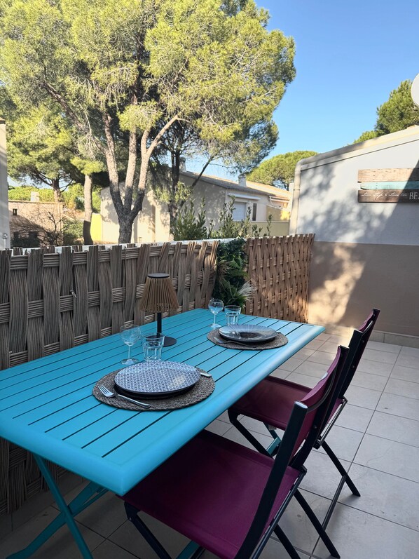An outdoor dining area with a blue table set for two, surrounded by wicker chairs.