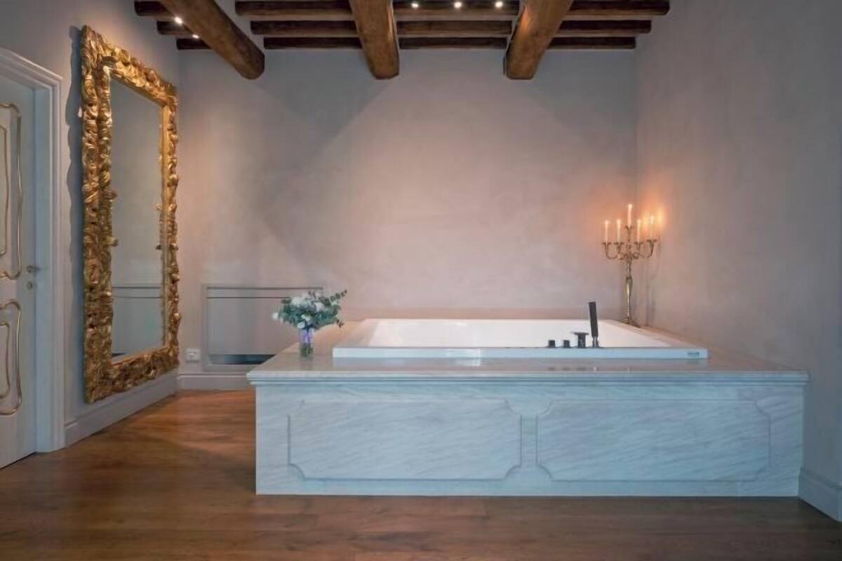 A modern bathroom with a freestanding bathtub, a large mirror with a gold frame, and a wall-mounted candelabra.
