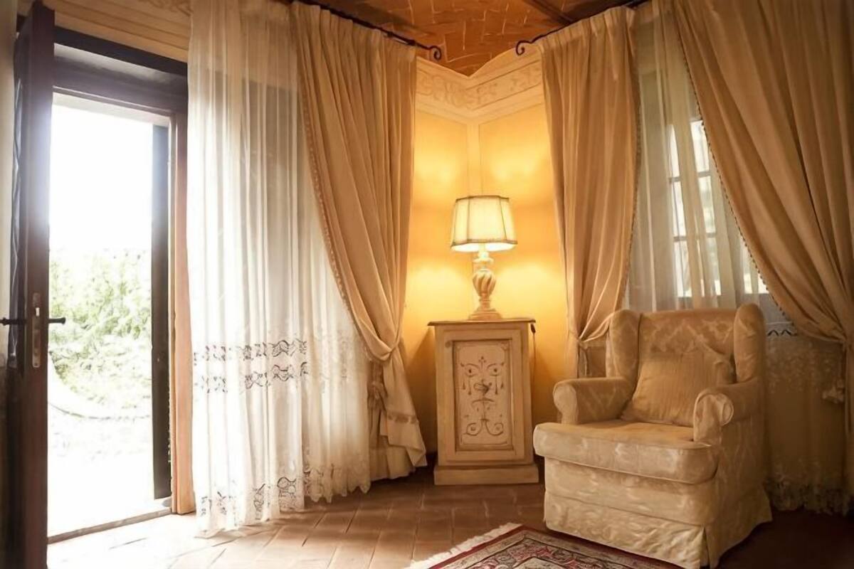 A room with a beige armchair, a small table with a lamp, and a door leading outside.