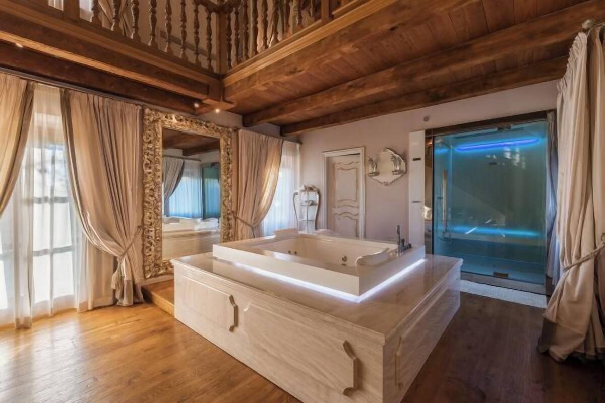 A spacious bathroom with a large bathtub, wooden ceiling beams, and a glass shower enclosure.