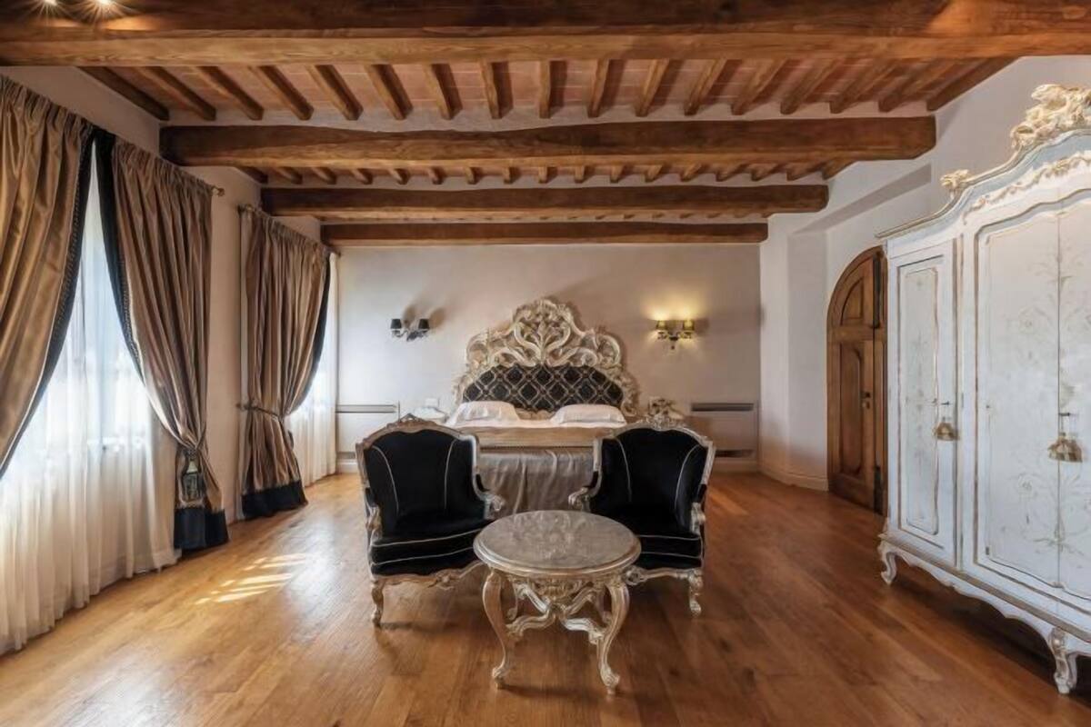 A room with a bed, two chairs, a table, and a cabinet.