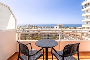 A balcony with two chairs and a table, overlooking a cityscape and the sea. - Catalonia Oro Negro (Playa de las Americas)